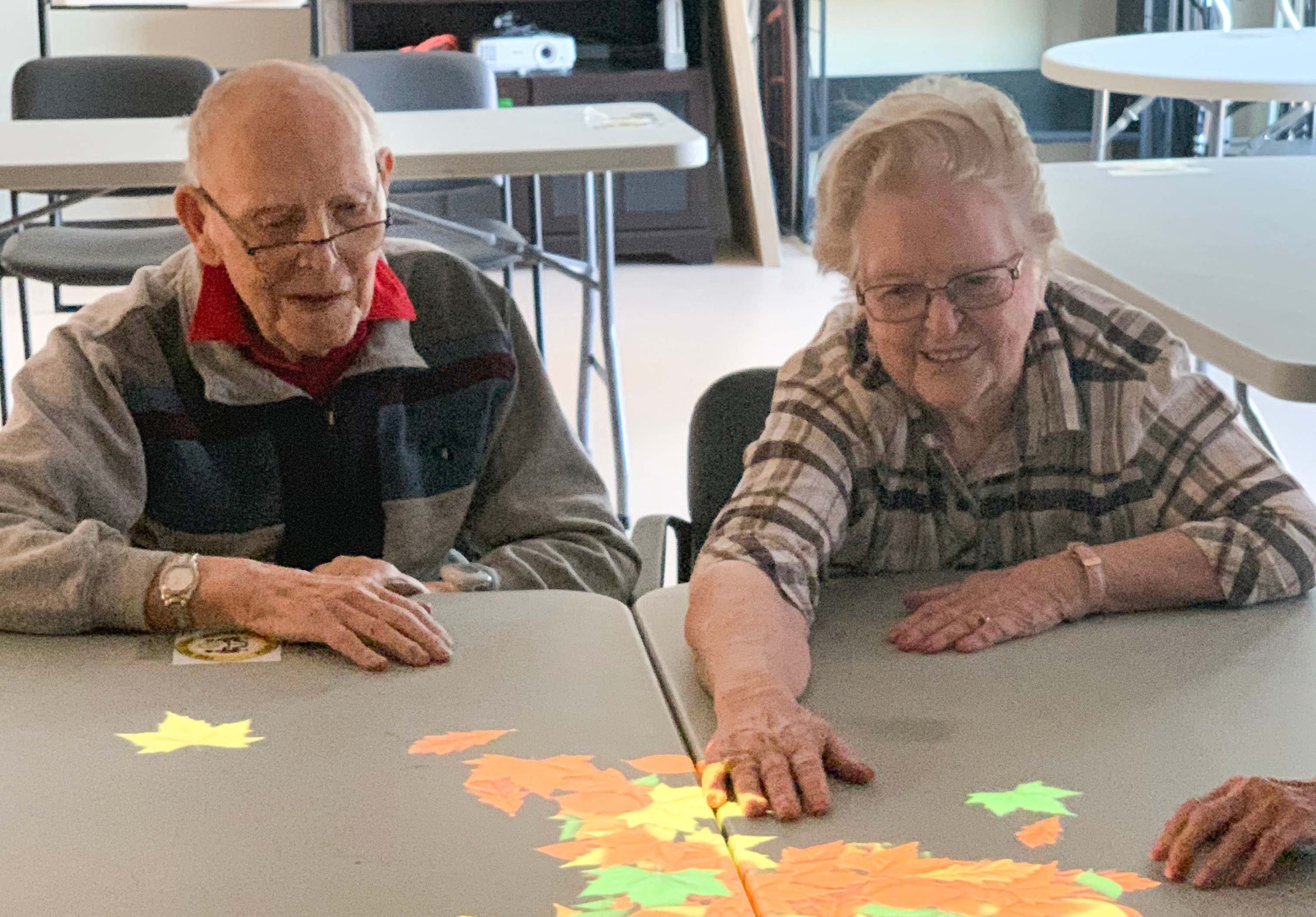 Two elderly Covenant residents play with the Tovertafel display on a table